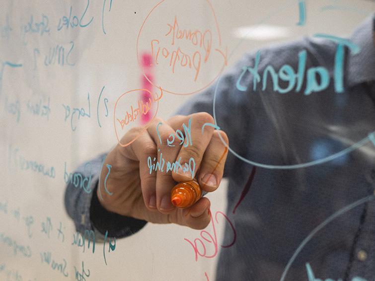 Een man die met een stift op een glazen whiteboard schrijft. 