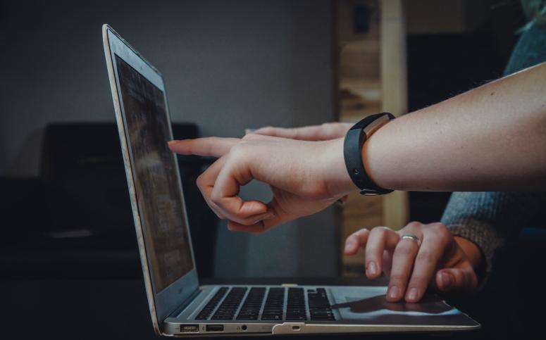 Een persoon met een smartwatch die wijst naar een apple laptop.